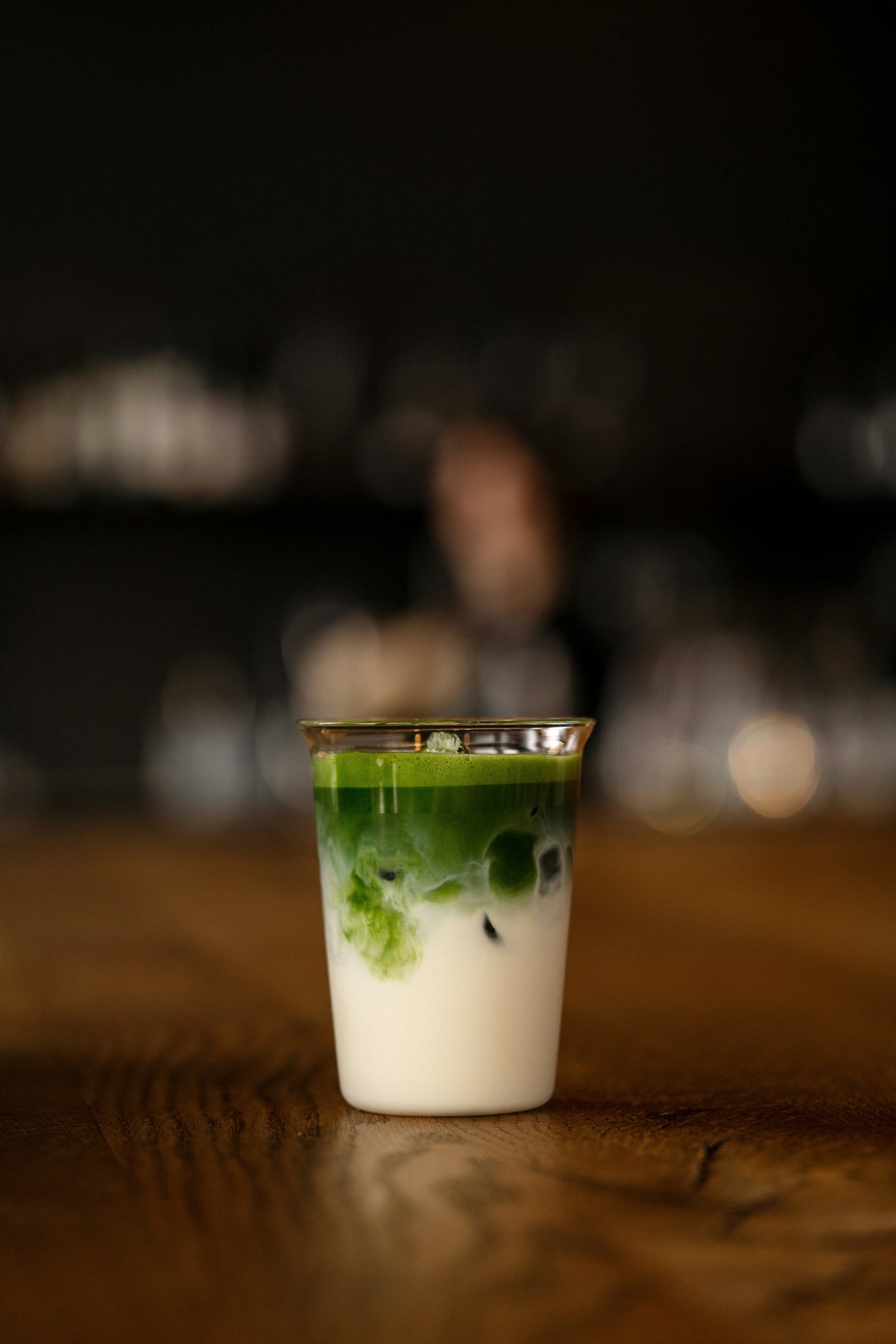Iced matcha latte in a clear glass on a wooden table with dark background