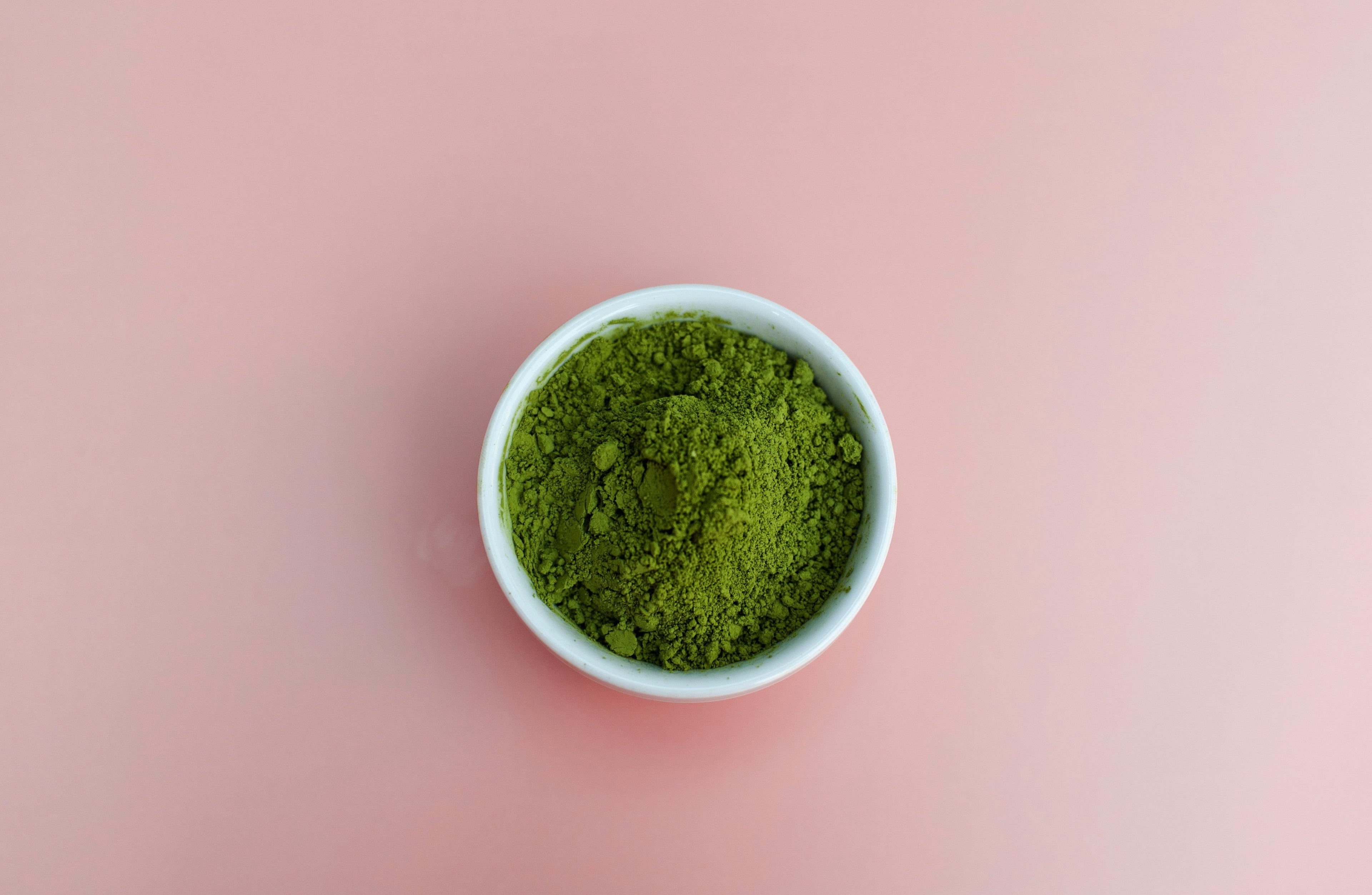 Ceremonial grade matcha powder in a white bowl on a pink background