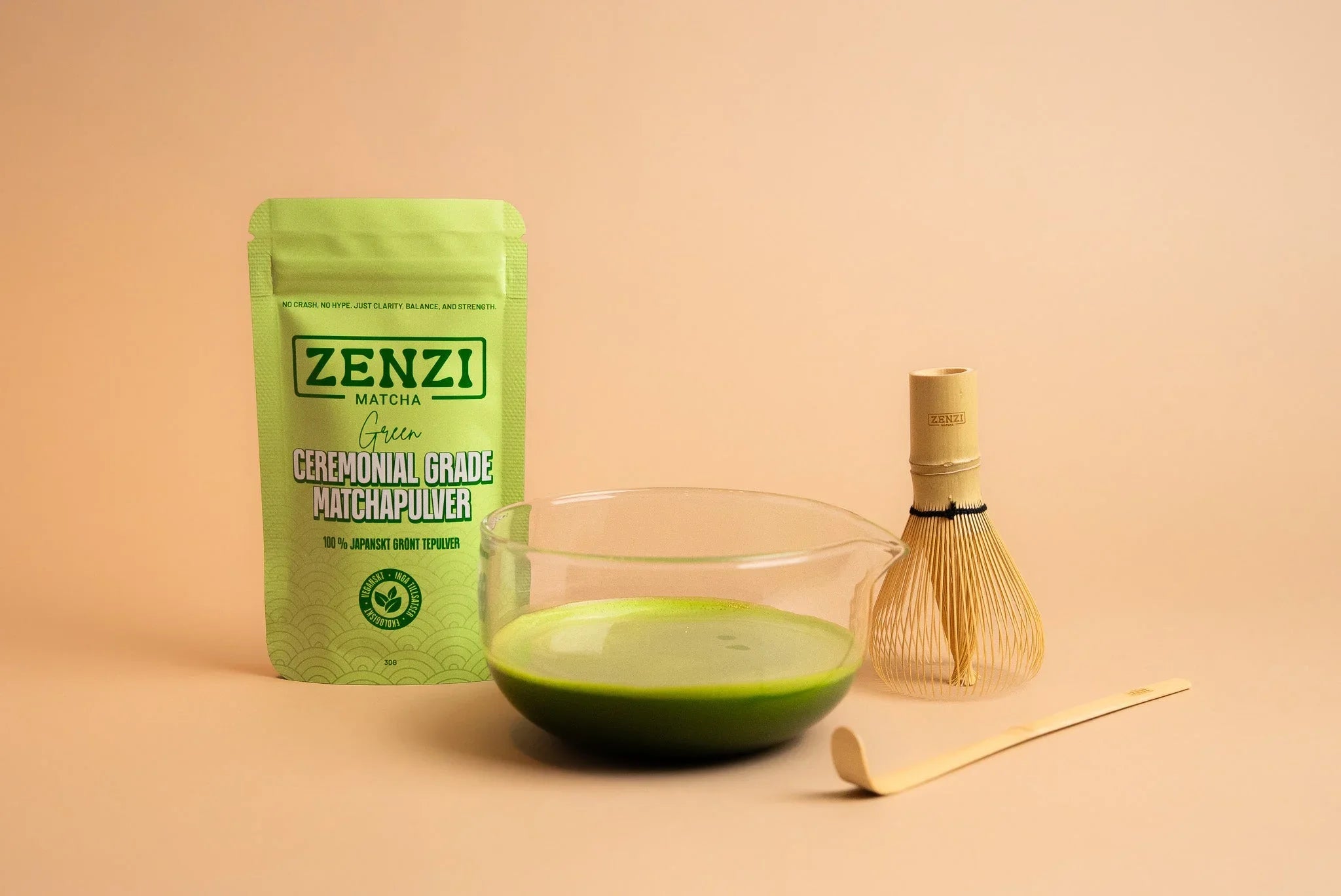 Ceremonial grade matcha powder pouch, matcha bowl, bamboo whisk, and scoop on beige background