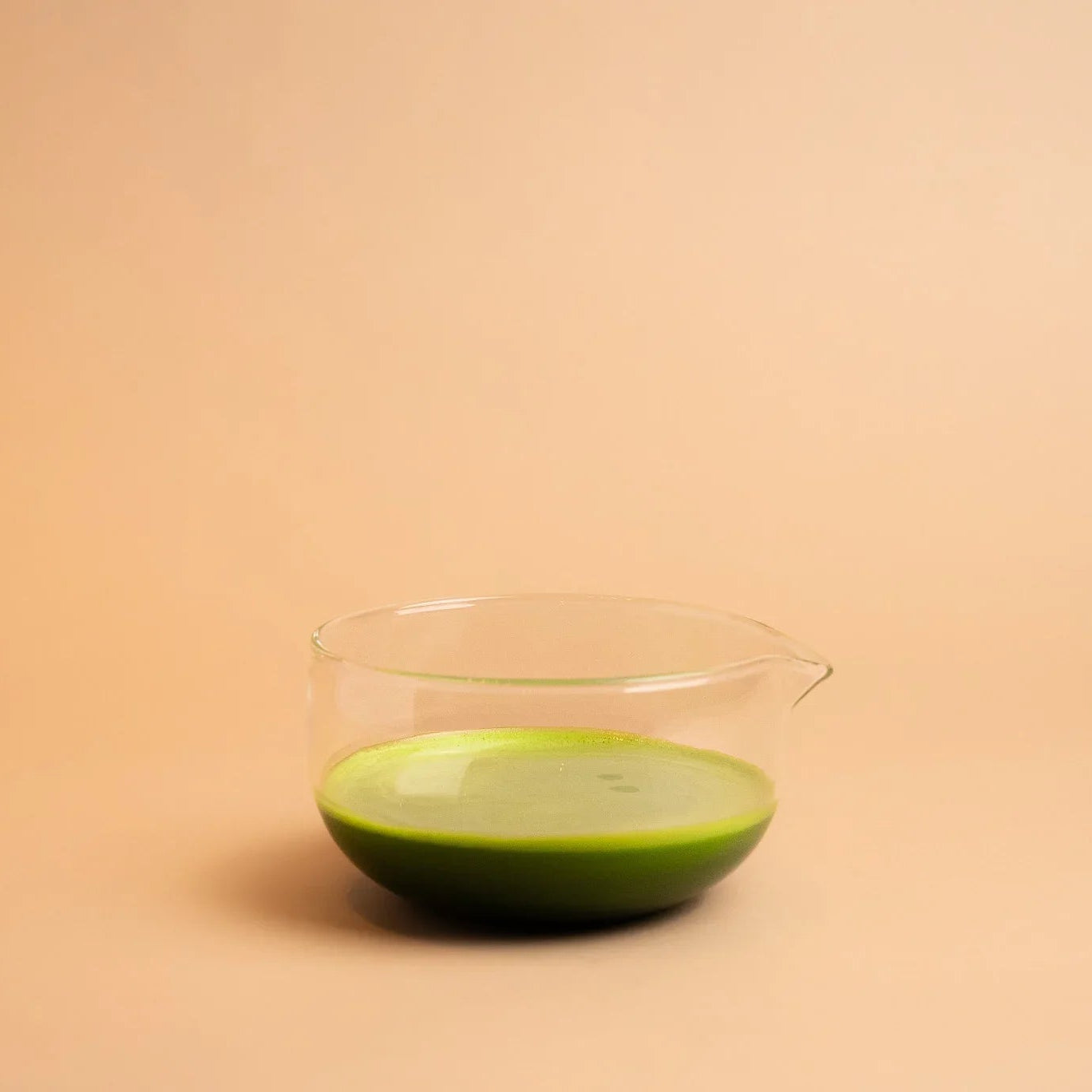 Ceremonial grade matcha tea in a clear glass bowl on a neutral background